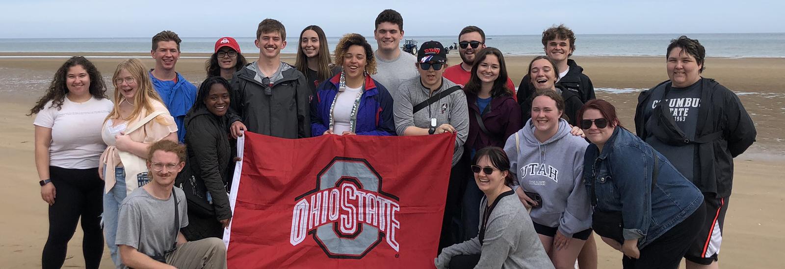 Students standing on Omaha Beach holding the Ohio State flag